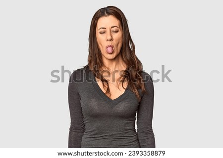 Elegant middle-aged Caucasian woman in studio setting funny and friendly sticking out tongue.