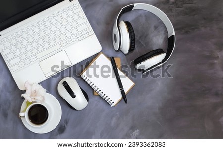 On the office table there is a laptop, computer mouse, notepad, pen, headphones, glasses, accessories for working in the office.  Space for copying text, top view.  Cup of coffee, coffee break.