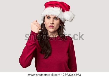 Young woman in Santa hat and red sweater showing fist to camera, aggressive facial expression.