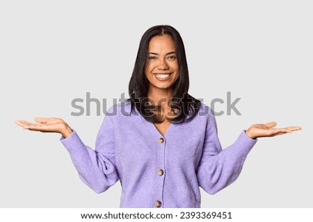 Young Filipina with long black hair in studio makes scale with arms, feels happy and confident.