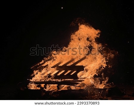 A campfire at campsite that provide light, warmth and heat for cooking. Campfires are a popular feature of camping. Dark background seen with pallete burning Royalty-Free Stock Photo #2393370893