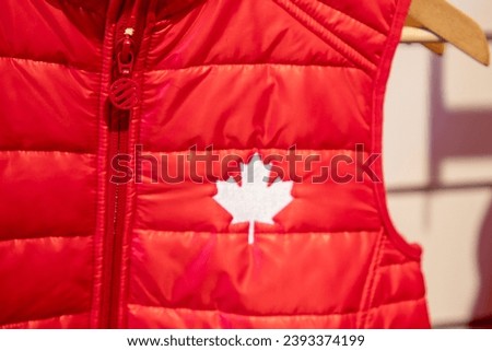 logo of Canada flag with sign maple leaf on the chest of a red winter vest jacket 