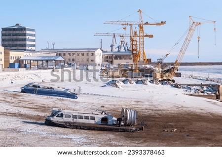 Hovercraft on the landing site at the commercial and passenger port in winter. Harbor cranes in the background. Snow and mud on a sunny day. Winter tourism concept. Royalty-Free Stock Photo #2393378463