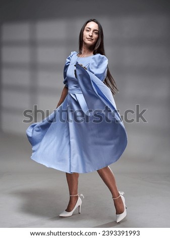 Full length studio portrait of a beautiful Hispanic woman in blue dress with a window projection shadow on background