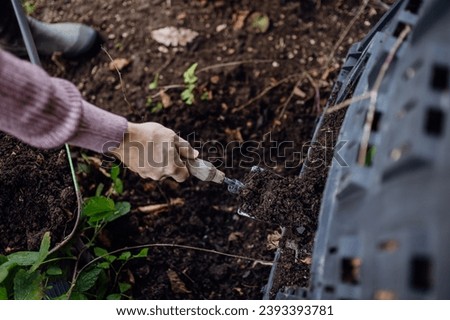 Girl removing compost from a composter in the garden. Concept of composting and sustainable organic gardening. Royalty-Free Stock Photo #2393393781