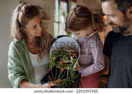 Girl helping parents put kitchen waste, peel and leftover vegetables scraps into kitchen compostable waste. Concept of composting kitchen biodegradable waste. Royalty-Free Stock Photo #2393393785