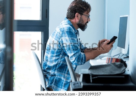 Adult business man work at office with mobile phone and desktop computer. Job and technology for modern people lifestyle. Smart working at home. Mature male sit down and look monitor