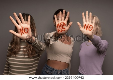 Three women boldly display "NO MEANS NO" written on their palms, symbolizing consent and empowerment Royalty-Free Stock Photo #2393400943