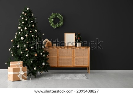 Beautiful Christmas tree with gifts and wooden dresser near dark wall. Banner for design