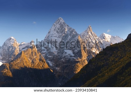 Sharp mountain peaks partially covered with snow and surrounded by rays of sun under a picturesque blue sky after dark, sunset or sunrise in the mountains in winter