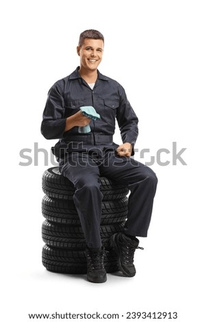 Auto mechanic worker sitting on a pile of tires and holding cloth isolated on white background Royalty-Free Stock Photo #2393412913