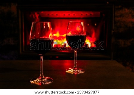 Two glasses of red wine on a background of a burning fireplace. Romantic evening near the fireplace