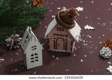 Cozy winter background. Wooden figure of house with traditional Christmas decor. New Year props, hard light, dark shadow, dark brown backdrop, copy space