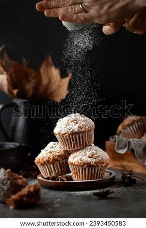 Woman's hand sprinkling icing sugar over homemade cinnamon muffins on black background. 