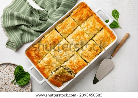 Spanakopita, homemade Greek savory spinach pie. It contains cheese feta, chopped spinach, green, egg, layered in phyllo or filo pastry. Top view. Royalty-Free Stock Photo #2393450585