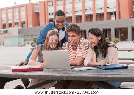 Group multi-ethnic smiling teenage students using laptop while looking information for an academic project outdoors. Meeting of diverse university young people enjoying while watching educational Royalty-Free Stock Photo #2393451559