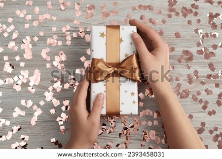 Christmas present. Woman with gift box and confetti at wooden table, top view