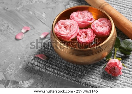 Tibetan singing bowl with water, beautiful roses and mallet on grey textured table, space for text