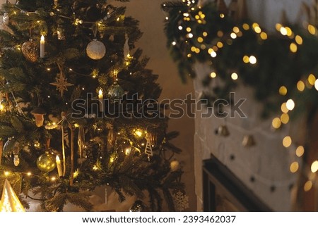 Stylish illuminated christmas tree with vintage baubles and festive decorated fireplace with golden lights in evening scandinavian room. Atmospheric christmas eve. Merry Christmas!