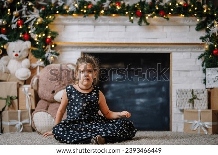 A little girl in a black dress with stars in a Christmas atmosphere. The girl is happy for Christmas. Christmas decorations. She is offended because she doesn't like taking pictures