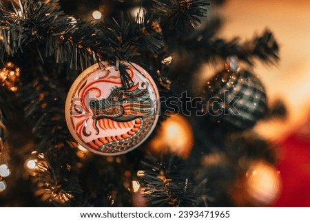 Festive shiny Christmas ball with the image of a dragon hanging on a Christmas tree with golden garland lights. Decorated spruce branches Royalty-Free Stock Photo #2393471965