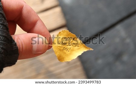 Fingers holding a small autumn leaf with Happy Thanksgiving Day written on it Royalty-Free Stock Photo #2393499783