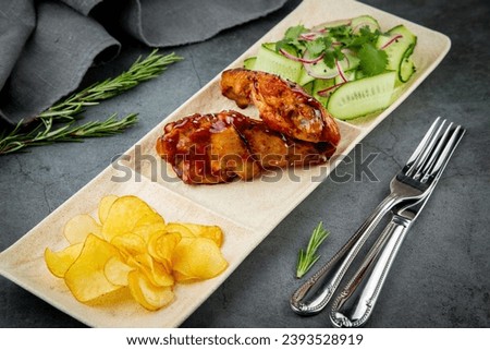 European dish. Chicken in sauce, with fried potatoes and cucumber salad, herbs and onions. dark background side view