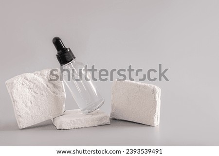 A beautiful transparent bottle with a pipette with an enhancering cosmetic product leaned on a white brick slice. Natural cosmetics. Front view