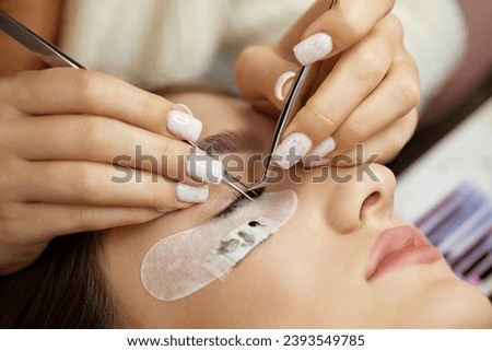 Beautiful female face during lash extension procedure in salon. Fake eyelashes Royalty-Free Stock Photo #2393549785