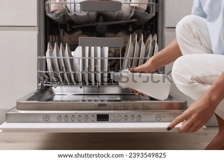 female hand pours rinse aid into the dishwasher compartment in modern white kitchen Royalty-Free Stock Photo #2393549825