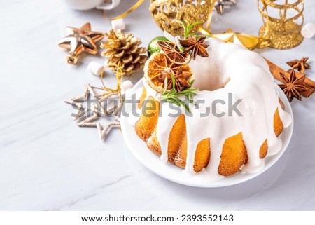 Christmas bundt cake decorated with sugar icing, orange and rosemary. Traditional Christmas and New Year baked dessert, vanilla sponge fruit cake, in white xmas decorated background