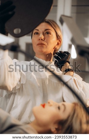 Beauty expert is holding mirror and showing result of drawn eyebrows to the client. Eyebrows microblading concept. Beauty salon consultations during pandemic of corona virus. High quality photo