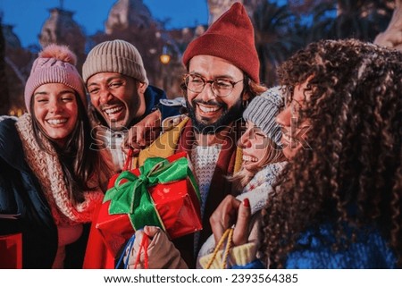 Group of best friends smiling giving a decorated xmas gift. Merry christmas. Excited people with a santa present with ribbon at festive eve. Man having a noel surprise on december traditional party Royalty-Free Stock Photo #2393564385