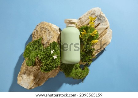 Green plastic bottle unbranded placed on blocks of stone with green moss and yellow flower on blue background. Natural concept for advertising and product promotion, mock up