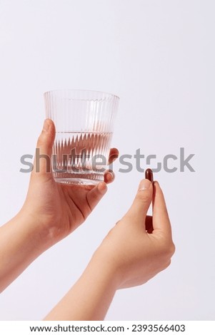 Front view of a glass of water in one hand and a capsule in the other on a white background. Using dietary supplements helps the body get enough nutrients. Medicine concept. Royalty-Free Stock Photo #2393566403
