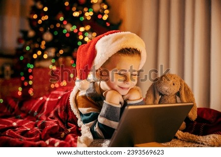 A child is watching christmas cartoons at home on christmas eve while smiling at tablet.