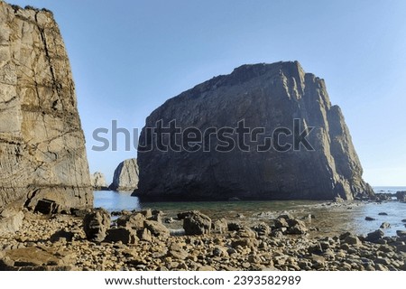 rocky coastline with large cliffs under a clear blue sky and calm deep blue water