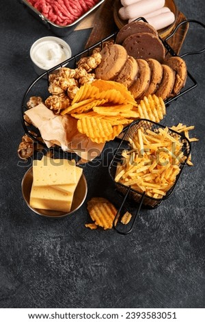Saturated and trans. Unhealthy food. Sausage, potato, meat, cheese, popcorn, cookies, cream on dark background. Copy space. Royalty-Free Stock Photo #2393583051