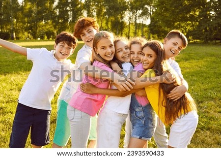 Children have fun and make friends at the summer camp. Group of kids spending time outdoors together. Bunch of happy girls and boys hugging each other in a green sunny park Royalty-Free Stock Photo #2393590433