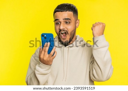 Happy excited Indian Hindu man guy use smartphone typing browsing shouting say wow yes found out great big win good news lottery goal achievement celebrating success, winning play game on yellow