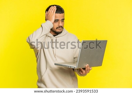Displeased Indian man use laptop notebook typing browsing working, loses becoming surprised by lottery bad results news fortune lost game fail computer virus. Arabian guy isolated on yellow background