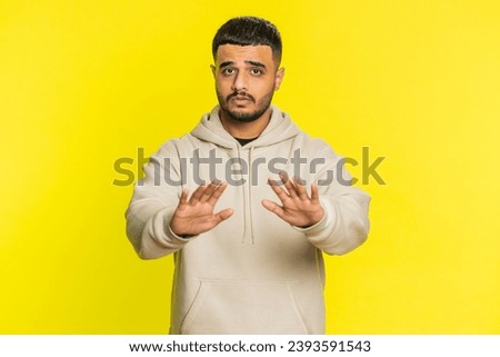 Hey you, be careful. Strict Indian man warning with admonishing hands gesture, saying no, be careful, scolding and giving advice to avoid danger, disapproval sign. Guy on yellow studio background Royalty-Free Stock Photo #2393591543