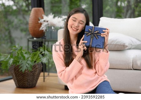 Attractive beautiful Asian woman holding a gift box while sitting on the sofa in the bedroom Smiling young woman holds a Valentine's Day gift from her boyfriend, lover. Happy Valentine's Day