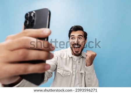 Portrait of a brunette man animate and joyful looking on the phone blogger with a beard taking selfies, on a blue background in a white T-shirt and jeans, copy space