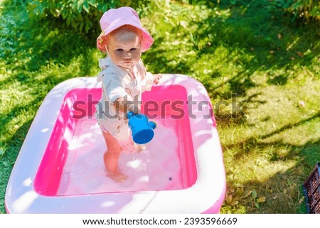 Cute baby child girl plays in an inflatable pink pool in summer