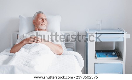 Senior patient rests while lying on the bed, recovering in modern hospital ward. Hospitalization. Treatment and healing. Coronavirus and pandemic concept Royalty-Free Stock Photo #2393602375