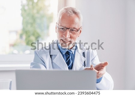 Telemedicine. Senior doctor making video call or live video on social network with patient or student while sitting on modern office in hospital. Online treatment Royalty-Free Stock Photo #2393604475
