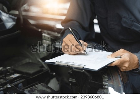Auto check up and car service shop concept. Mechanic writing job checklist to clipboard to estimate repair quotation to client at workshop garage. Royalty-Free Stock Photo #2393606801