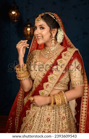 Stunning Indian bride dressed in traditional bridal lehenga with heavy gold jewellery and veil smiles tenderly in studio lighting. Wedding fashion and lifestyle. Royalty-Free Stock Photo #2393609543