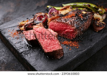 Barbecue dry aged wagyu roast beef steak with BBQ chili and onion rings served as close-up on a charred black wooden board  Royalty-Free Stock Photo #2393610003
